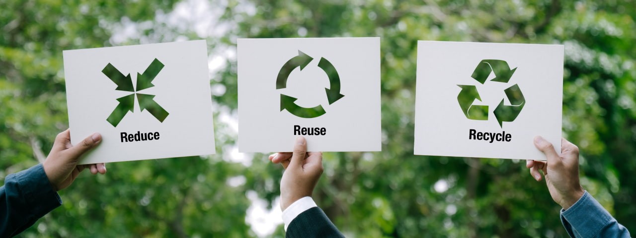 Hands holding up signs that say Reduce Reuse Recycle.